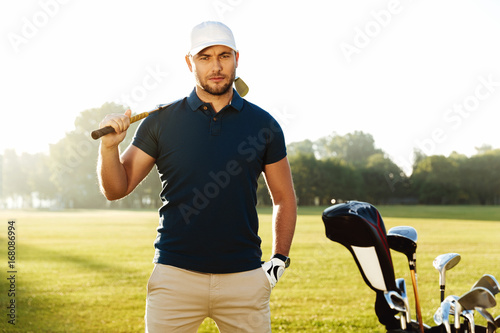 Handsome confident male golfer standing with golf club photo