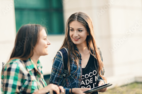Friends sharing their vacation stories after the first day of school. Attractive girl listening to her friend with a beautiful smile on face. Looking prettier in the outfit and makeup. Back to school