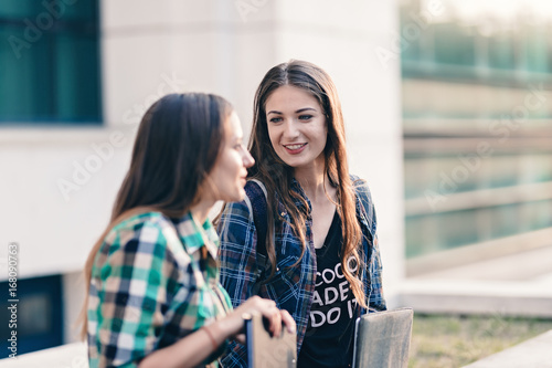 Friends sharing their vacation stories after the first day of school. Attractive girl listening to her friend with a beautiful smile on face. Looking prettier in the outfit and makeup. Back to school