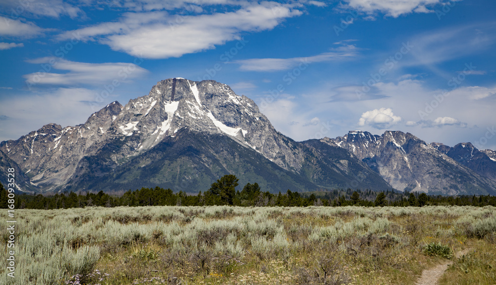 The mountain peaks of Grand Teton National Park, Wyoming with glaciers and snow fields lake, blue color, sky, landscape with an active blue and cloudy sky