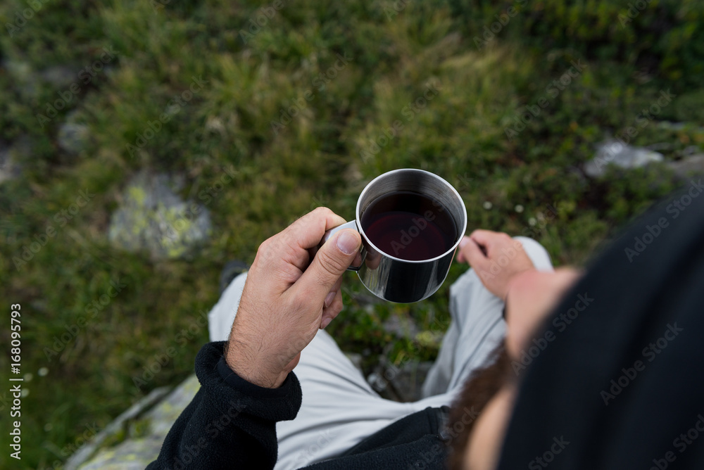 Young adult man drink tea from metal cup in mountain at dawn in summer outdoor.