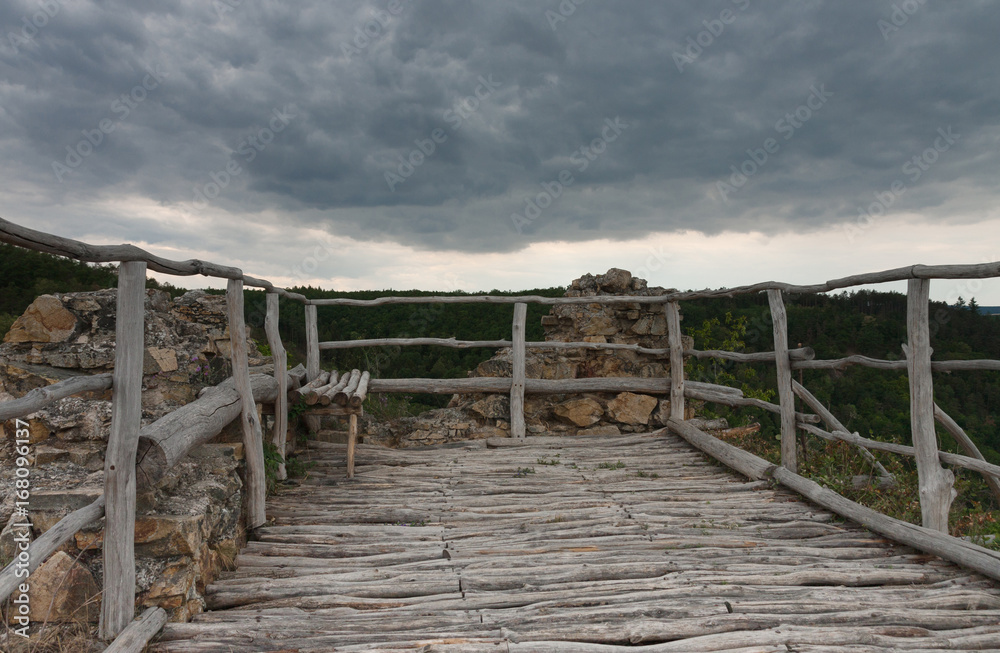 Wooden benche on castle ruins, in backgrounds is cloudy sky.
