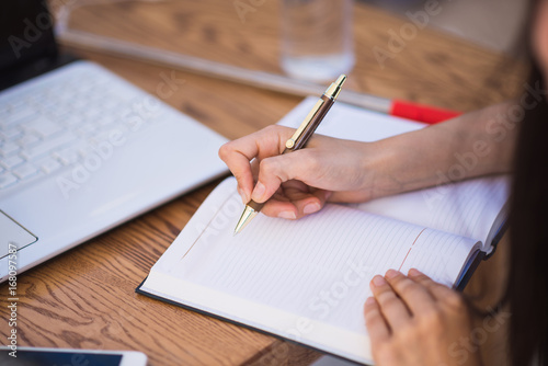 Close up opened notebook in which woman writes something by table