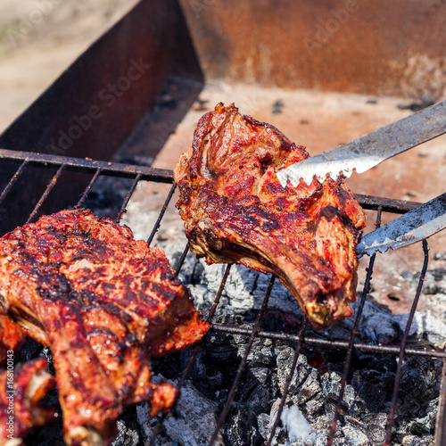 Grilled beef fillet ribs on bbq over charcoal. Roasted meat. Large pieces of grilled meat during cooking. Veal on the bone. The man flips the meat with tongs.