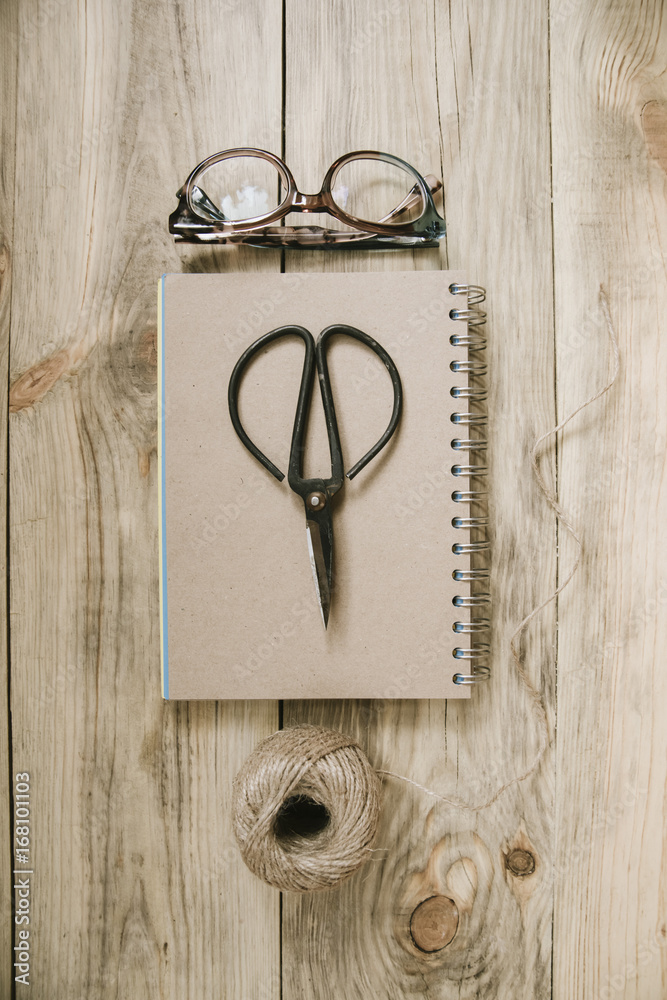 Crafting scissors, glasses, cardboard notebook, twine, laptop on the old rustic table background Crafting scissors, glasses, cardboard notebook, twine, laptop on the old rustic table background