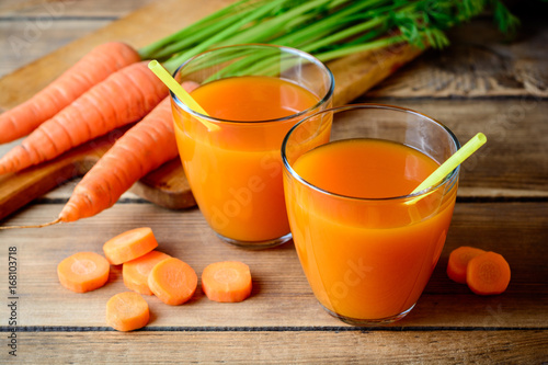 Fresh carrot juice in glasses on rustic wooden table.