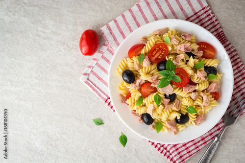 Fusilli pasta salad with tuna, tomatoes, black olives and basil on gray stone background