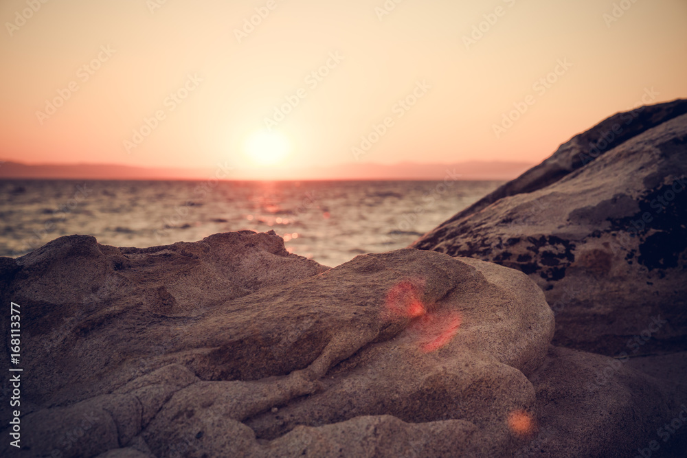 Dawn seascape behind big stone / Beautiful beach in Greece while sun rising over the sea