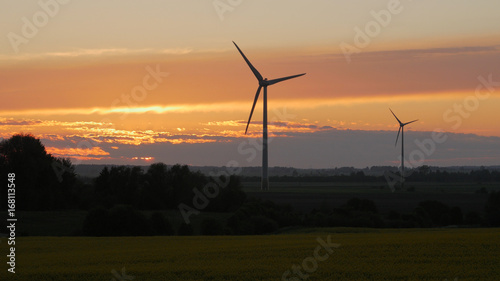 Wind turbines farms with rays of light at sunset in the background.