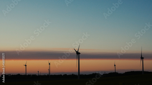 Wind turbines farms with rays of light at sunset in the background.