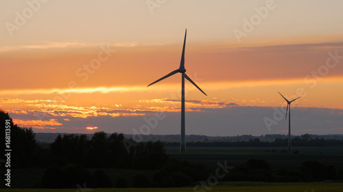 Wind turbines farms with rays of light at sunset in the background.