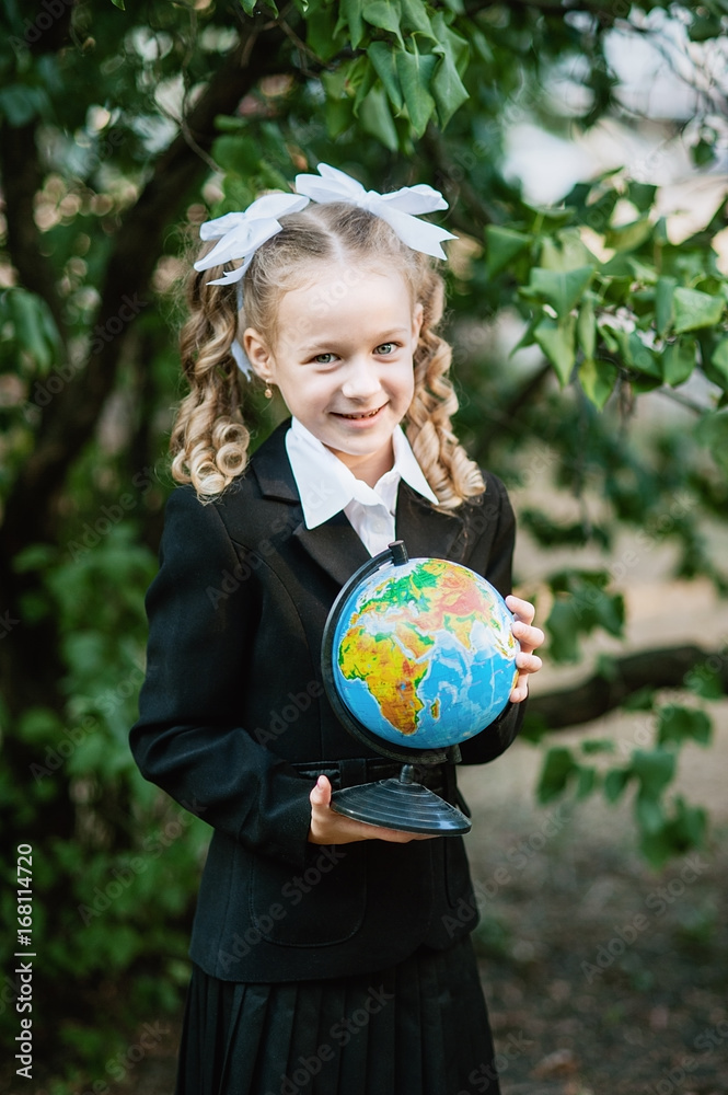 Portrait of a beautiful young first-grader with the globe with russian text. in a festive school uniform Portrait of a beautiful young first-grader with the globe with russian text. in a festive school uniform