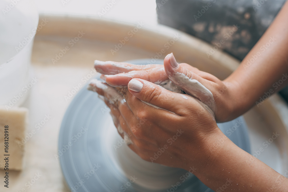 Hands of young female potter works with white clay on pottery wheel