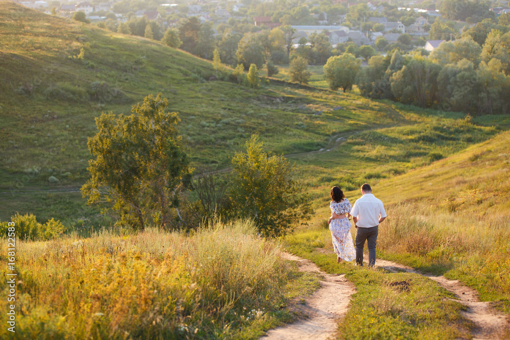 Young couple walking on a hills. Tender holding each other. Young family on a summer walk. Love and tenderness