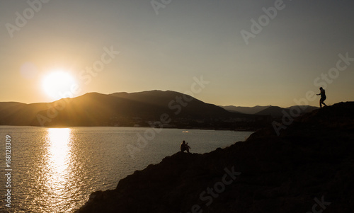 Silhouettes of people on a cliff against the sea and the setting sun