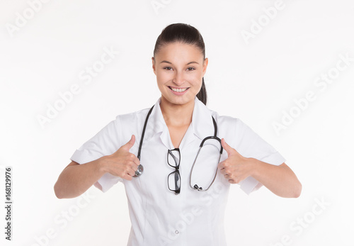 Portrait of a beautiful young woman doctor in white coat with stethoscope holding thumbs up.