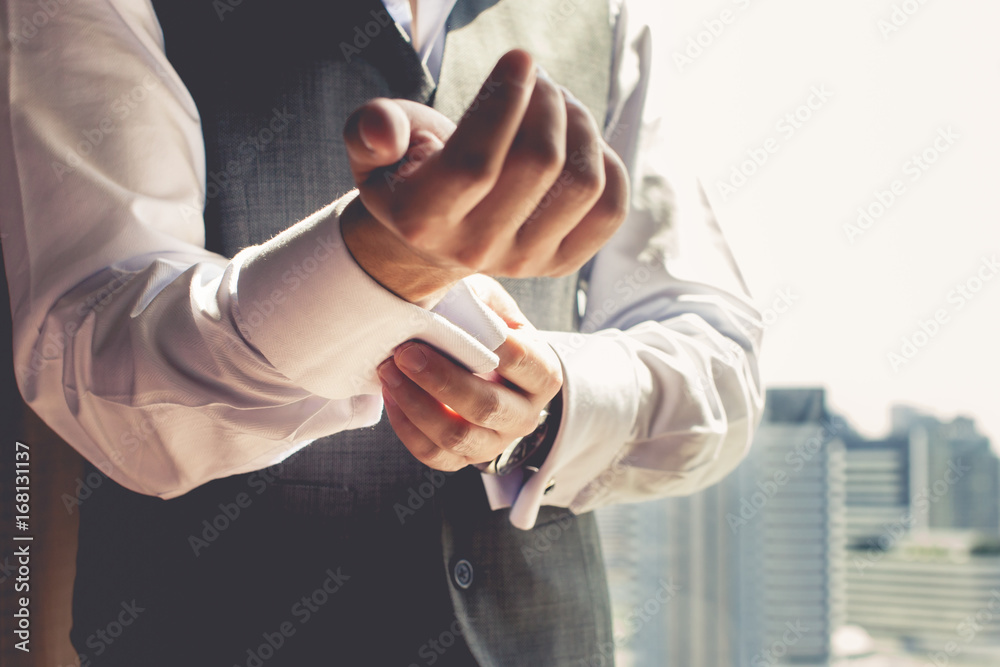 Fototapeta premium A groom putting on cuff-links as he gets dressed in formal wear .Groom's suit