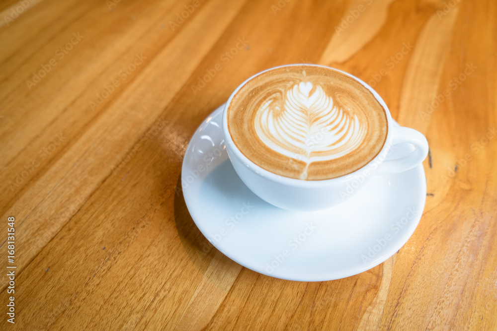 A white cup of hot latte art coffee on the wooden table in coffee cafe A white cup of hot latte art coffee on the wooden table in coffee cafe