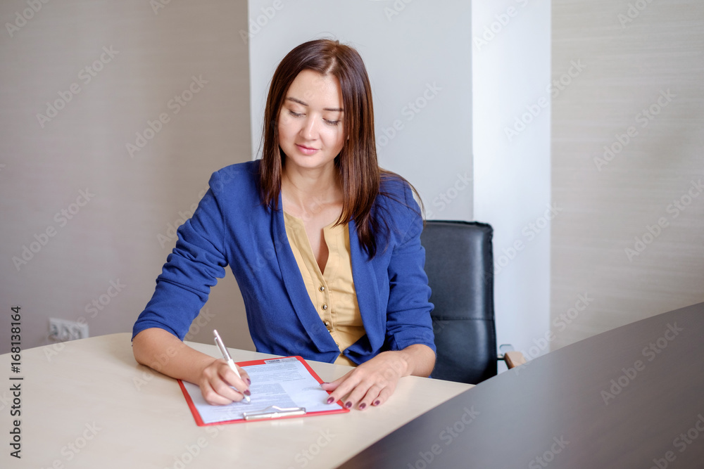 Young businesswoman working at desk in office, taking notes into personal calendar, smiling. Young businesswoman working at desk in office, taking notes into personal calendar, smiling.