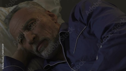 Bearded old male lying in bed awake unable to fall asleep at night sleeplessness photo