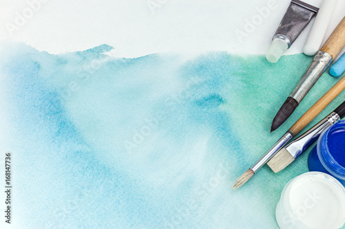 artist paintbrushes and paints over abstract hand painted watercolor background on textured paper photo