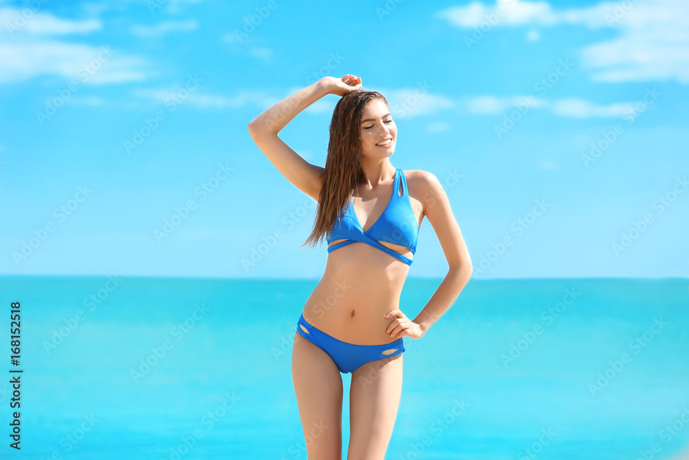 Beautiful young woman in bikini near sea on summer day