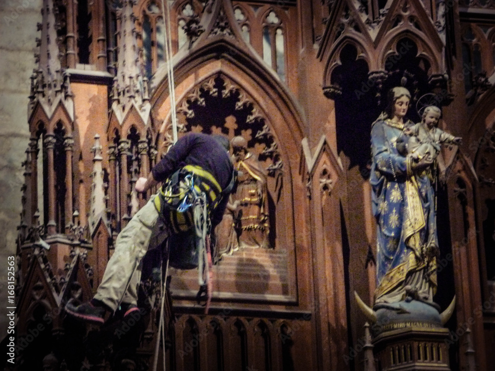 Worker hanging from harness on rope repairs church interior Worker hanging from harness on rope repairs church interior