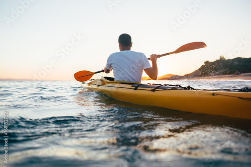 Man kayaker paddling the kayak at sunset sea