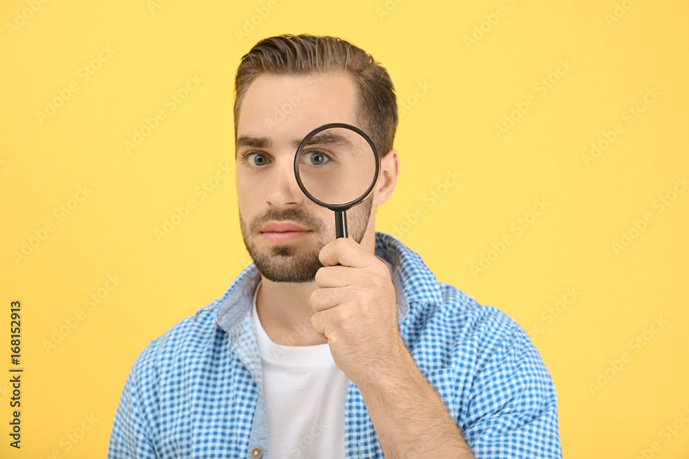 Handsome young man with magnifier on color background Handsome young man with magnifier on color background