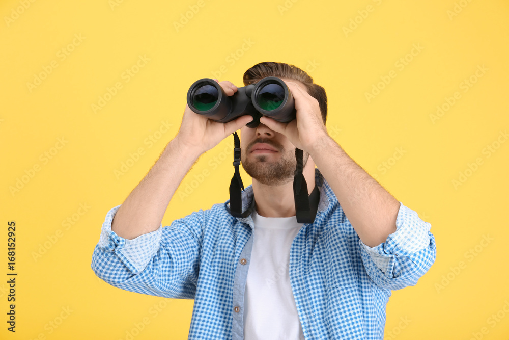 Handsome young man with binocular on color background Handsome young man with binocular on color background
