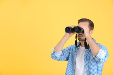Handsome young man with binocular on color background