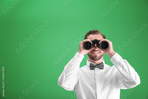 Handsome young man with binocular on color background