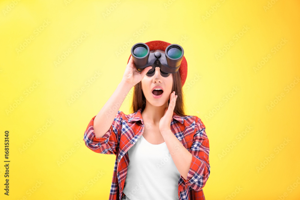 Beautiful young woman with binocular on color background