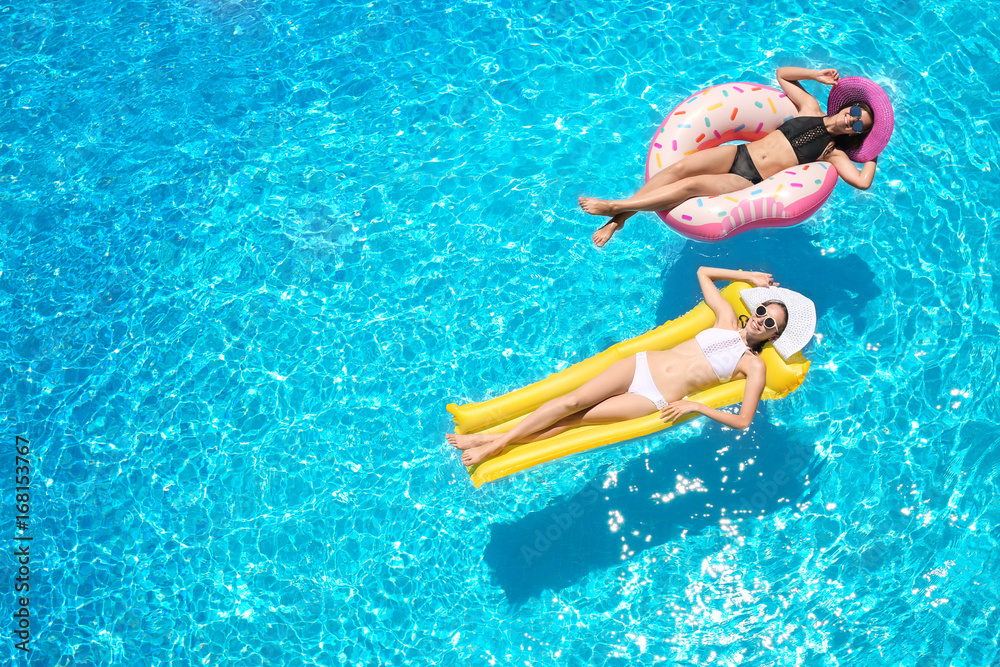 Beautiful young women with inflatable donut and mattress in blue swimming pool