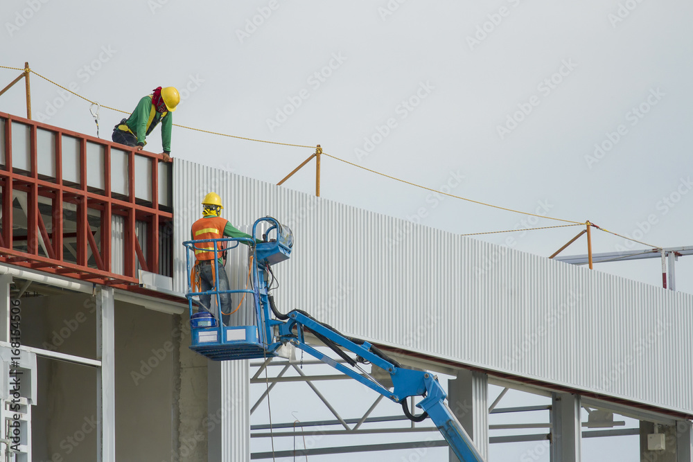 Workers in a baskets are installing sheet, building a factory. Workers in a baskets are installing sheet, building a factory.