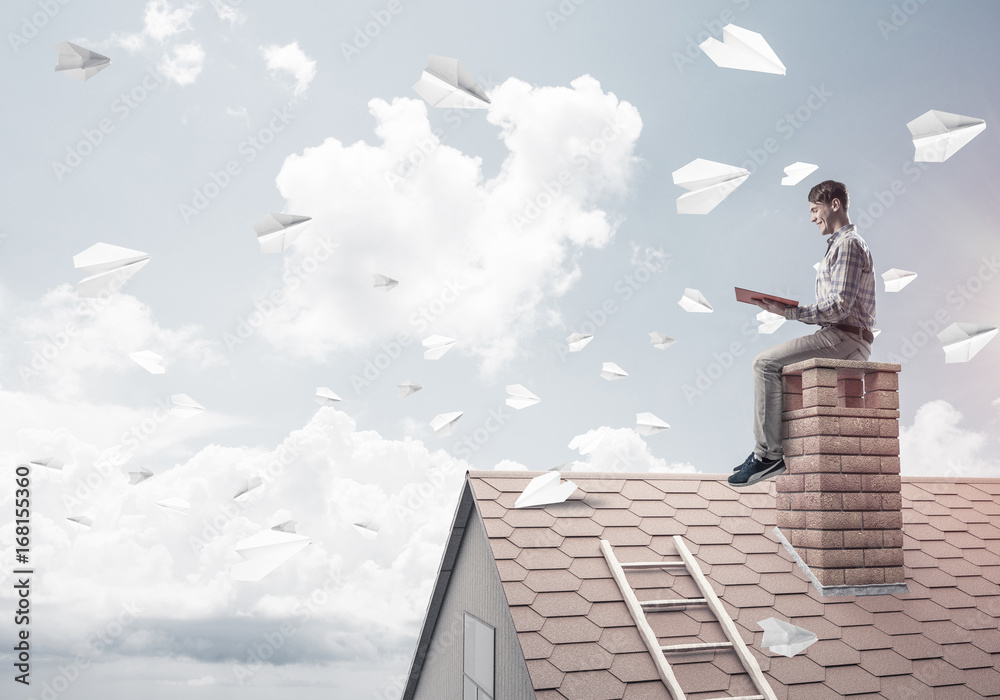Man on brick roof reading book and paper planes flying in air Man on brick roof reading book and paper planes flying in air