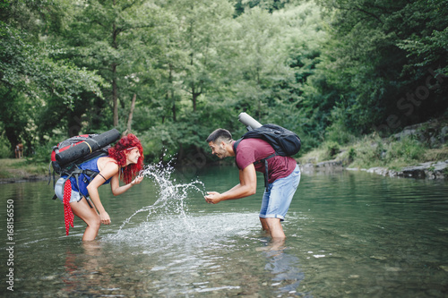 Fototapeta Naklejka Na Ścianę i Meble -  Happy young hikers couple enjoying in adventure. They camping and having fun while walking through the wild mountain river.