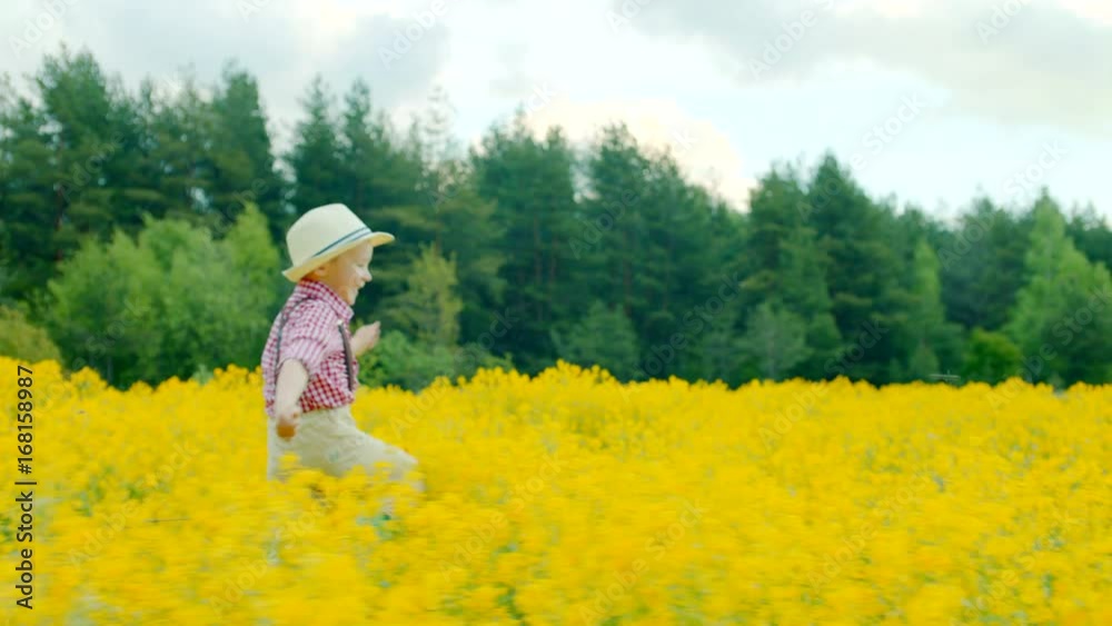 Happy little boy in straw hat running at the flowering glade Happy little boy in straw hat running at the flowering glade