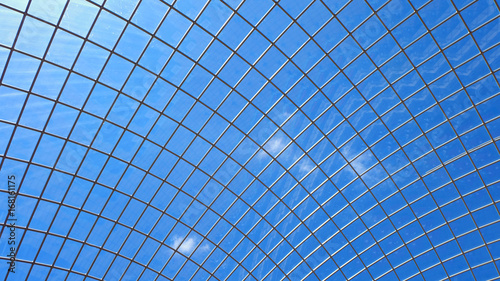 Bilde på lerret A dome shaped glass ceiling with metal support structure beams or frame with blue sky and a little white clouds in the background