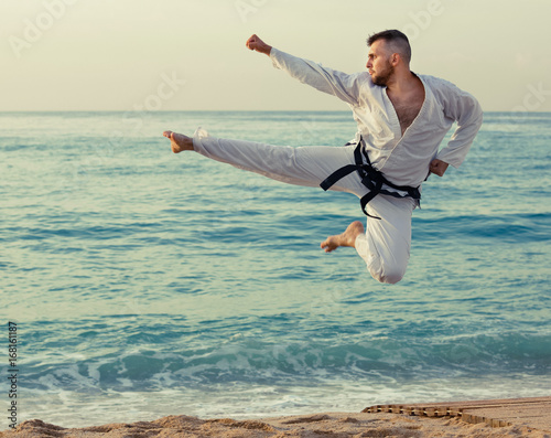 Guy doing karate poses at sunset sea shore