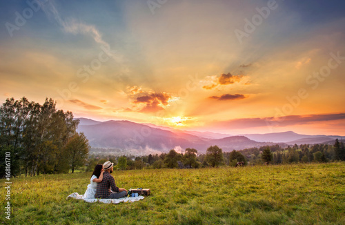 nature and people concept - happy loving couple sitting on plaid in field. background mountain