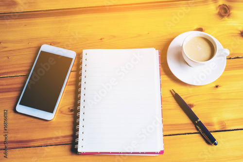 on wooden table in coffee shop interior near mobile phone and cup of coffee book pen and smartphone , blank space on book