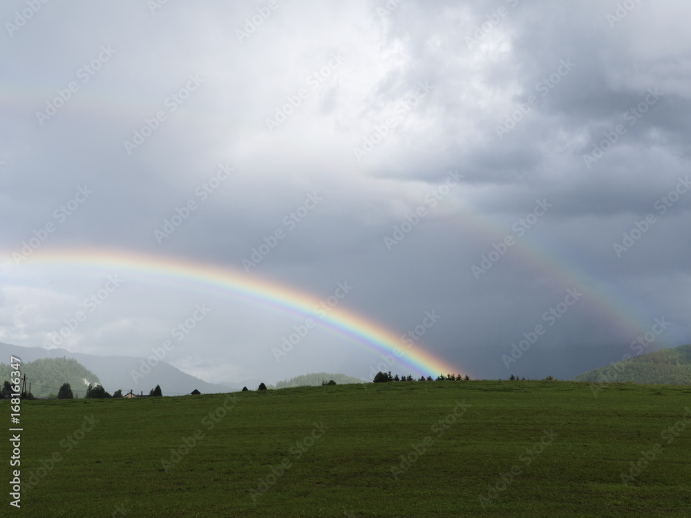 Alpine landscape with beautiful rainbow. Mountains, meadows and pastures. Rainy weather. Idyllic virgin and clean landscape. Salzburg vacation landscape. Mystical foggy evening scene with sun bow.