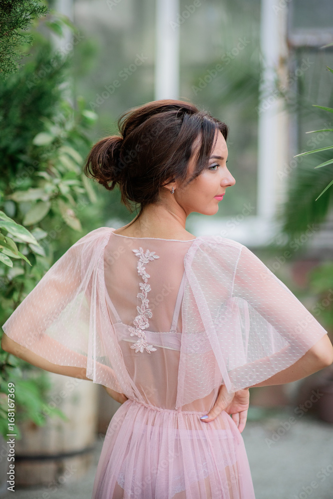 Seductive woman in pink lace robe and lingerie stands in the garden