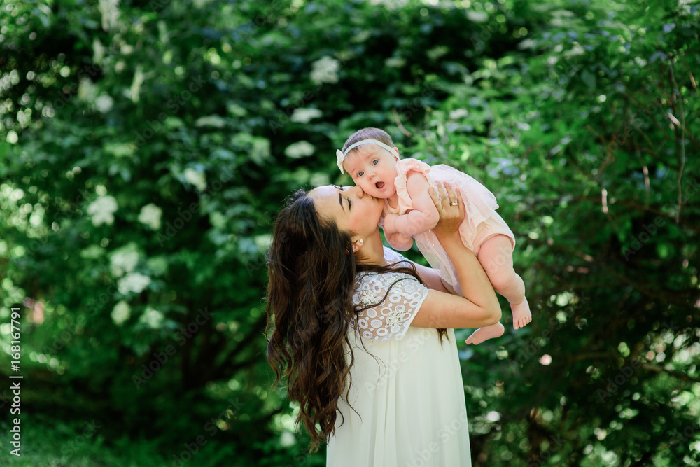 Pretty brunette woman in white dress poses with her little daughter in the garden Pretty brunette woman in white dress poses with her little daughter in the garden