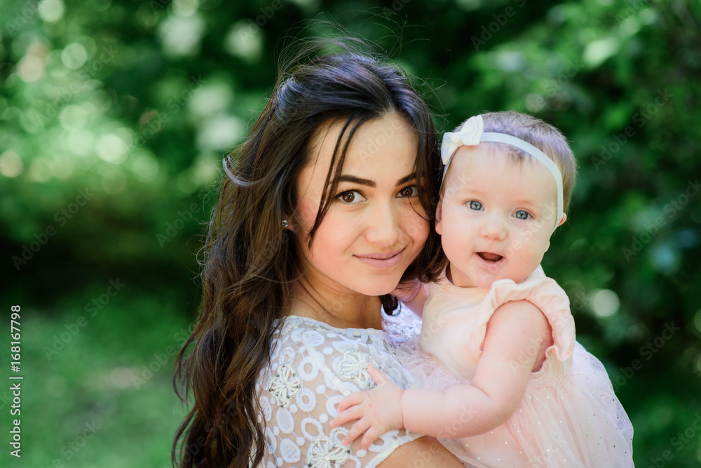 Pretty brunette woman in white dress poses with her little daughter in the garden Pretty brunette woman in white dress poses with her little daughter in the garden