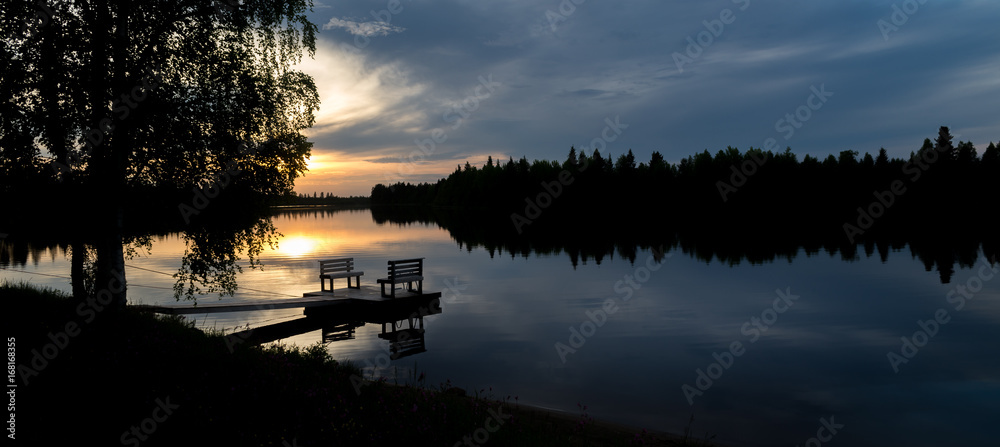 Obraz premium Empty footbridge with a bench on a lake in Lapland. Midnight sun in summertime.