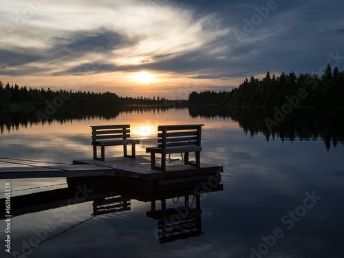Empty footbridge with a bench on a lake in Lapland. Midnight sun in summertime.