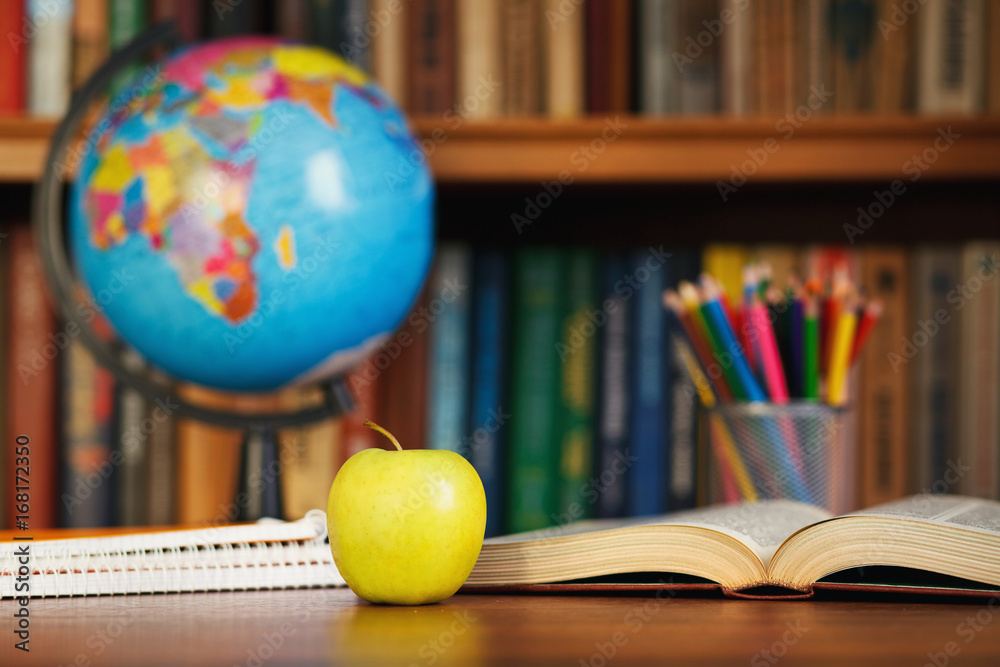 Globe, organizer, an apple and an open book on the table on the background library Globe, organizer, an apple and an open book on the table on the background library