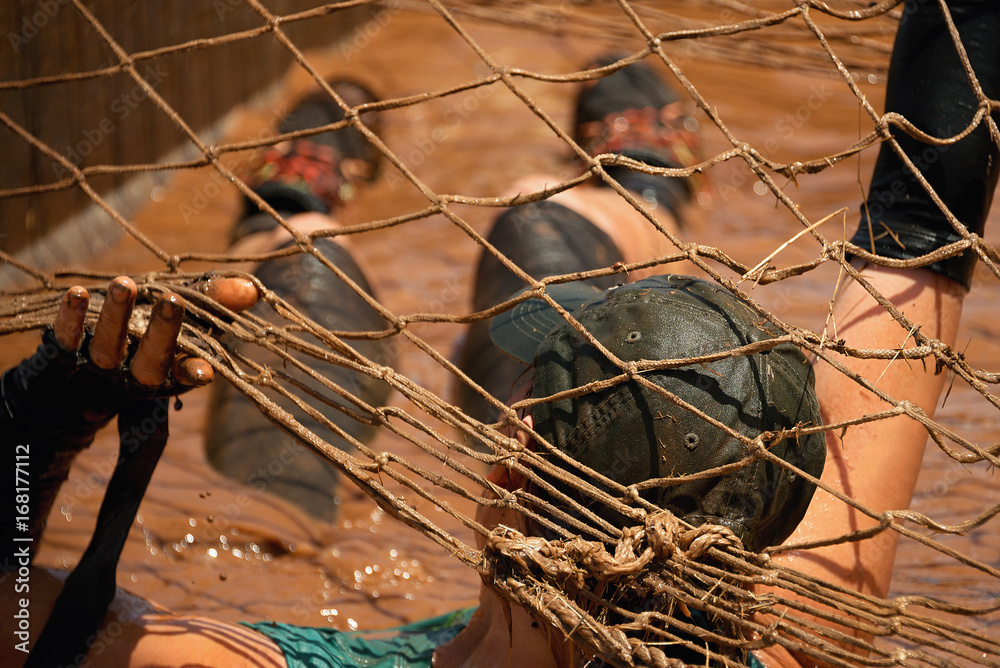 Mud race runners.Woman covered with mud fighting to get out of a net in the obstacle race Mud race runners.Woman covered with mud fighting to get out of a net in the obstacle race